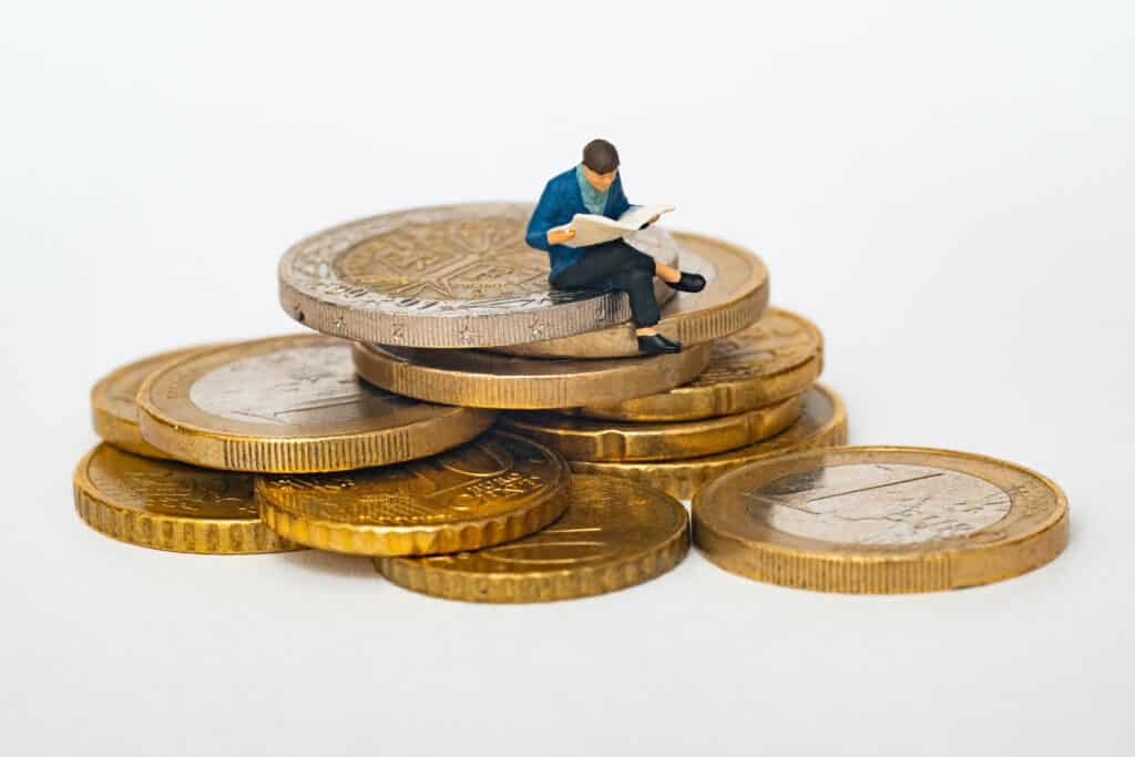 imagen de un personaje encima de unas monedas leyendo un libro, en relación con la educación financiera y el ahorro.